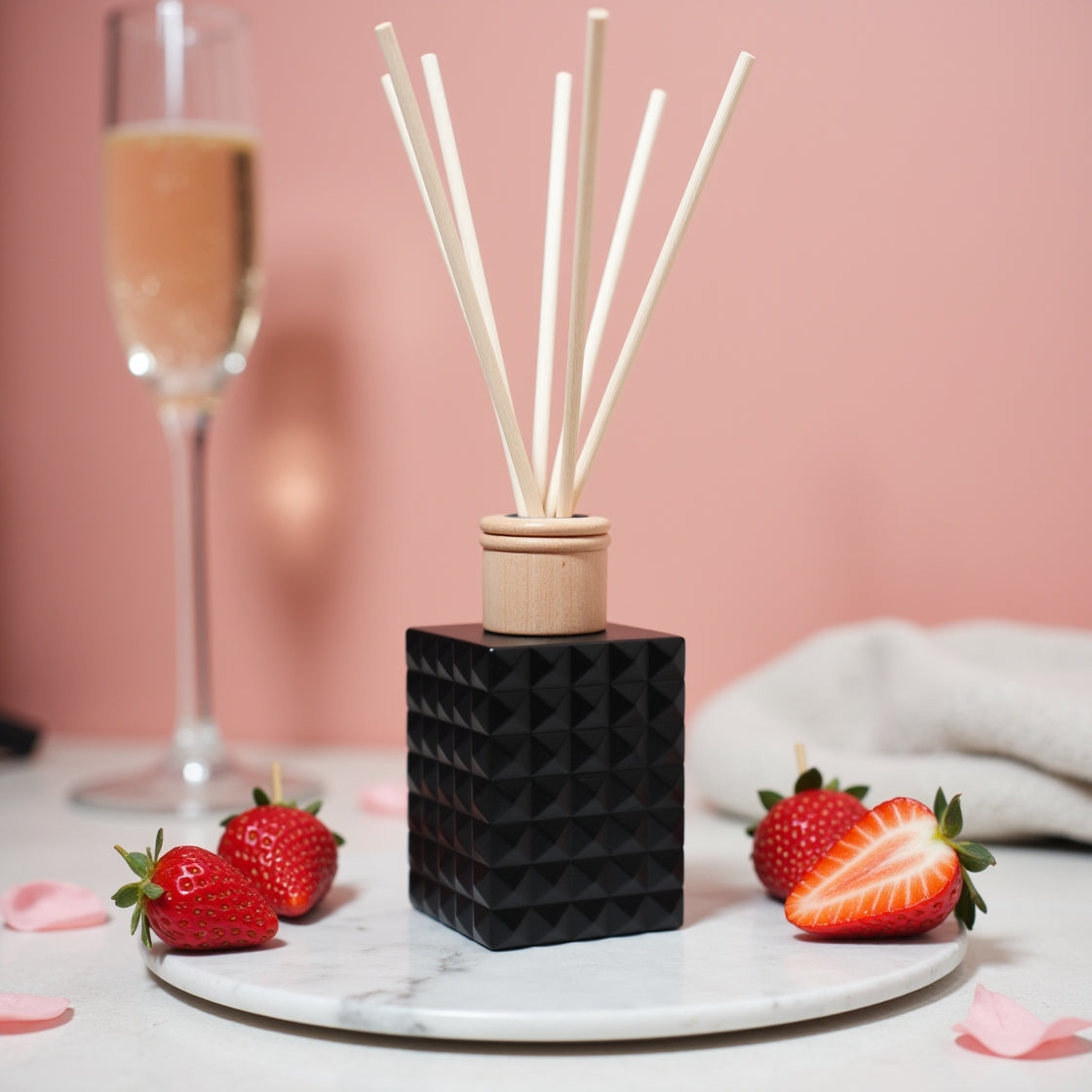 A romantic Champagne & Strawberry scented reed diffuser in a matte black bottle.